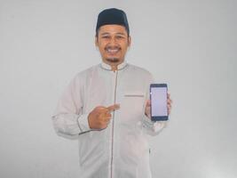 moslem asiatisk man leende och pekande till tom mobil telefon skärm den där han håll foto