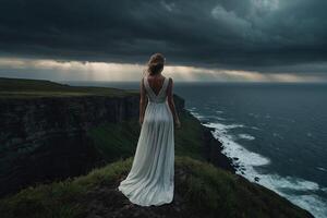 en kvinna i en vit klänning står på en klippa utsikt de hav foto