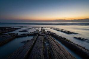 ai genererad en lång exponering fotografera av en klippig strandlinje på solnedgång foto