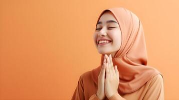 sydöst asiatisk kvinna bär scarf är bön- och leende på orange bakgrund foto