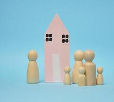 trä- hus och miniatyr- figurer av en familj på en blå bakgrund. de begrepp av försäljning och uppköp verklig egendom foto