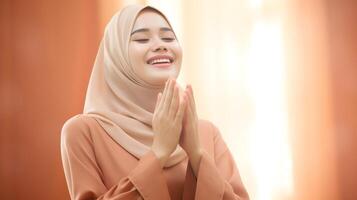sydöst asiatisk kvinna bär scarf är bön- och leende på orange bakgrund foto