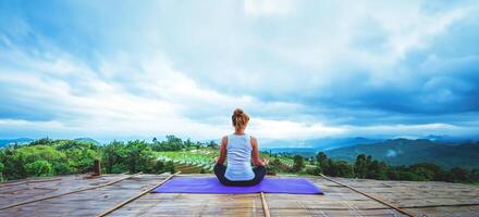 asiatisk kvinna koppla av i semestern. spela om yoga. på balkongen landskap naturfält foto