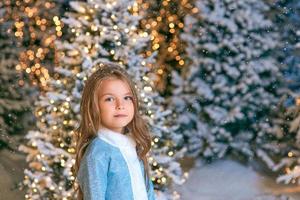 söt kaukasisk blond flicka promenader vinter jul skog med ljus. nytt år, sagokoncept foto
