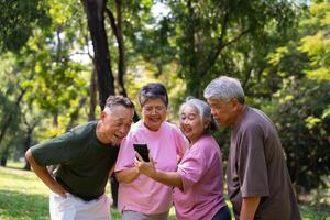 grupp av Lycklig senior pensionering använder sig av smartphone och skrattande utomhus på de parkera efter en träna och utgifterna tid tillsammans, begrepp handla om de äldre, anciennitet, och wellness åldring foto