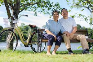 Lycklig och friska par asiatisk Sammanträde stol bredvid en cykel familj och vänskap livsstil, njutning av aktiva seniorer, och utomhus- aktivitet efter pensionering, hälsa vård försäkring begrepp foto