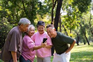 grupp av Lycklig senior pensionering använder sig av smartphone och skrattande utomhus på de parkera efter en träna och utgifterna tid tillsammans, begrepp handla om de äldre, anciennitet, och wellness åldring foto