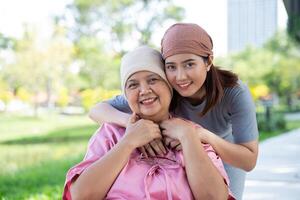 asiatisk försiktig vårdgivare eller sjuksköterska och kvinna med cancer är Sammanträde i en rullstol. i de trädgård. begrepp av Lycklig pensionering med vård från en vårdgivare och besparingar och senior hälsa försäkring. foto