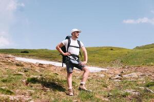 en skäggig resande med en ryggsäck på de topp av en berg. en turist med en ryggsäck står mot de bakgrund av en berg foto