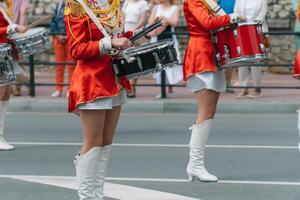gata prestanda av festlig Mars av trummisar flickor i röd kostymer på stad gata. ung flickor handelsresande i röd årgång enhetlig på de parad foto