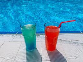 sommar slå samman fest, semester. blå och röd cocktails med is stå på sida slå samman, mot bakgrund av slå samman, blå vatten foto