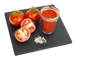 glas tomatjuice, mogna röda tomater på svart stenbricka