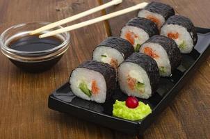 svart tallrik med rullar med lax på träbord. grön wasabi och sojasås. foto