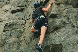 ung man i Utrustning håller på med sten klättrande utomhus. Träning område för utomhus- aktiviteter. extrem sport. foto