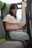 en flicka rider en tåg Sammanträde på de fönster. de flicka har roligt spelar på henne telefon medan reser förbi tåg. de passagerare är visning de Nyheter på hans smartphone. foto