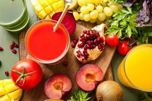 glasögon med hälsosam juice, frukt och grönsaker på färg trä bakgrund foto