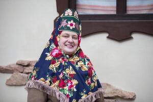 ett äldre ryska kvinna i en traditionell huvudbonad, kokoshnik, poser mot de bakgrund av en by hus. foto