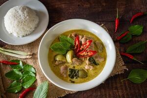 stängd upp traditionell thai kyckling grön curry med färsk vegetabiliska och ört i skål på trä- tabell, thai mat begrepp med jasmin ris foto