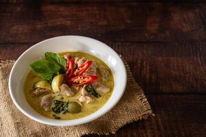 stängd upp traditionell thai kyckling grön curry med färsk vegetabiliska och ört i skål på trä- tabell, thai mat begrepp. foto