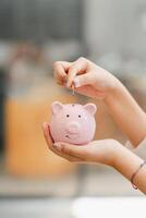 händer av en person införing en mynt in i en leende rosa nasse Bank, symboliserar besparingar och finansiell planera. foto
