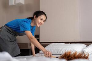 en kvinna asiatisk personal rengöring service, verktyg och hink för arbete. en ung kvinna rengöringsmedel med Produkter till rena en sovrum, damm av de säng foto