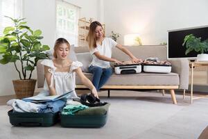 ung asiatisk kvinna förpackning kläder till de resväska. förberedelse för de sommartid semester. två kvinnor är planera en resa och portion till förbereda bagage till resa foto