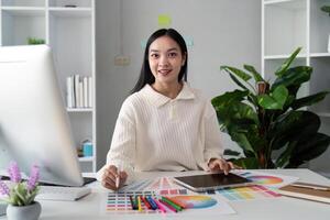 asiatisk kvinna frilans grafisk designer arbetssätt med Färg swatch prover och dator på skrivbord i Hem kontor, ung lady välja Färg gamma för ny design projekt foto