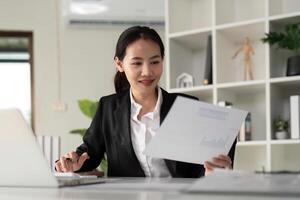ung företag kvinna asiatisk eller anställd bokföring bokföring dokument kontroll finansiell data eller marknadsföring Rapportera arbetssätt i kontor med bärbar dator. pappersarbete förvaltning foto