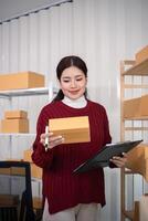 ung företag kvinna asiatisk arbetssätt uppkopplad e-handel handla på henne affär. ung kvinna sälja förbereda paket låda av produkt för leverera till kund. uppkopplad försäljning foto