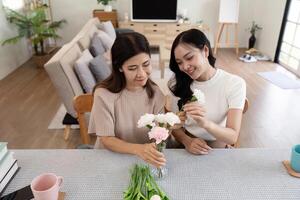 senior mor och vuxen dotter Lycklig på de tabell medan ordna blommor i en vas tillsammans. teknologi och livsstil begrepp. Lycklig tid tillsammans foto