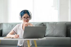 Lycklig ung kvinna Tonårs bär hörlurar skrivning notera. studerande uppkopplad inlärning klass studie uppkopplad ring upp zoom lärare med bärbar dator och bok foto