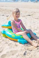 Lycklig flicka av europeisk utseende ålder av 5 Sammanträde och skrattande på ett uppblåsbar krokodil leksak på de strand sommar solig dag.familj sommar yrke begrepp. vertikal Foto. foto