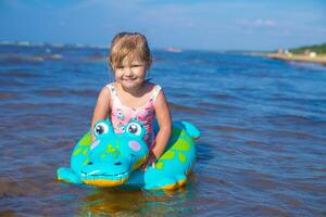 Lycklig flicka av europeisk utseende ålder av 5 simning på ett uppblåsbar krokodil leksak i de hav.barn lära sig till simma.lite bebis flicka med uppblåsbar leksak flyta spelar i vatten på sommar kall.familj sommar yrke koncept.kopia Plats. foto