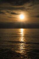 solnedgång, upplyst hav. en få moln i de himmel, ljus vågor rullande till de strand foto