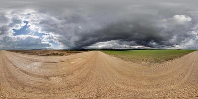 hdri 360 panorama på våt grus väg bland fält i vår otäck dag med storm moln i likriktad full sömlös sfärisk utsprång, för vr ar virtuell verklighet innehåll foto