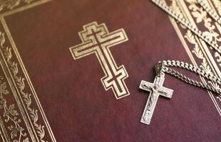 silver- halsband med krucifix korsa på kristen helig bibel bok på svart trä- tabell. be välsignelser från Gud med de kraft av helighet, som ger tur foto