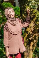 en förtäckt kvinna var stående Nästa till en träd med de skugga av de löv rätt på henne ansikte. foto