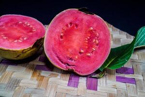 guava isolerat. guava frukt med röd kött med gulaktig grön hud och löv isolerat på en svart bakgrund med vävd bambu som en bas. foto