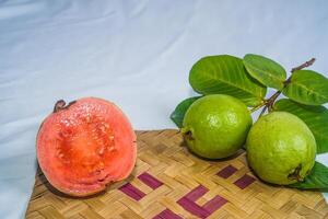 guava isolerat. samling av röd kött guava frukt med gulaktig grön hud och löv isolerat på en vit bakgrund med bambu matta. foto