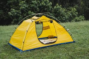 turist tält för tre människor, en plats till sömn i natur, en sovande väska lögner i de tält, metall båge ram, resten i de skog vandra. foto