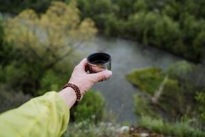 hand innehar en mugg, varm te till dryck i natur, armband på hand, helig rudraksha träd på de handled insvept i struntsak, termos i natur, njutning foto