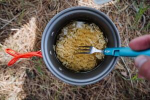 en turist äter spaghetti från en panorera med en gaffel, mat på en vandra, camping frukost i de skog, turist maträtter, en kompakt ljus pott, laga mat mat på en resa. foto