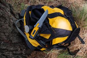 en vandring kniv för överlevnad i de skog lögner på en ryggsäck, en vandring kniv med en gul hantera, grå plast slida, en snodd för de hand. foto