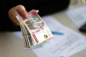 kvinna revisor hand ge knippa av många indonesiska rupiah pengar räkningar av ny serier foto