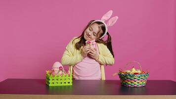 glad leende flicka kramas henne fylld kanin leksak och ägg, känsla stolt handla om henne handgjord målad påsk dekorationer. ung litet barn med kanin öron och flätor, festlig ornament. kamera b. foto