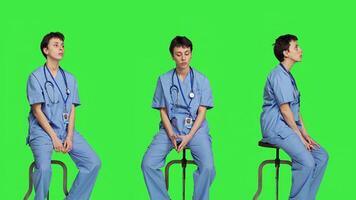 medicinsk assistent väntar för någon medan hon sitter på stol, känsla otålig och väntar för patienter till närvara kolla upp möten. sjuksköterska i scrubs mot grönskärm bakgrund. kamera a. foto