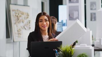 porträtt av arkitekt studerar 3d byggnad modell för mått, ser på tryckt maquette till Översätt mått i coworking Plats. asiatisk ingenjör arbetssätt på industriell konstruktion. foto