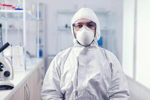 porträtt av trött forskare bär overall med skydd glasögon ser på kamera i medicin laboratorium. överarbetad forskare klädd i skyddande kostym mot invektion med coronavirus under global epidemi. foto