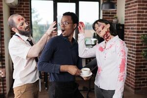 anställda bär zombie kostymer trams runt om med chef i kontor, låtsas till besitter honom. team ledare och medarbetare klädd som odöda varelser har roligt under halloween händelse på arbete foto