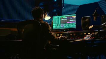 afrikansk amerikan audio ingenjör användningar kompressor och mixer i professionell studio, ändring volym nivå och ljud inställningar på en inspelning. musik produktion i kontrollera rum. kamera b. foto